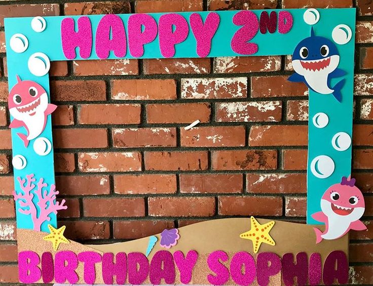 a birthday sign made to look like a shark and dolphin with bubbles on it, sitting in front of a brick wall