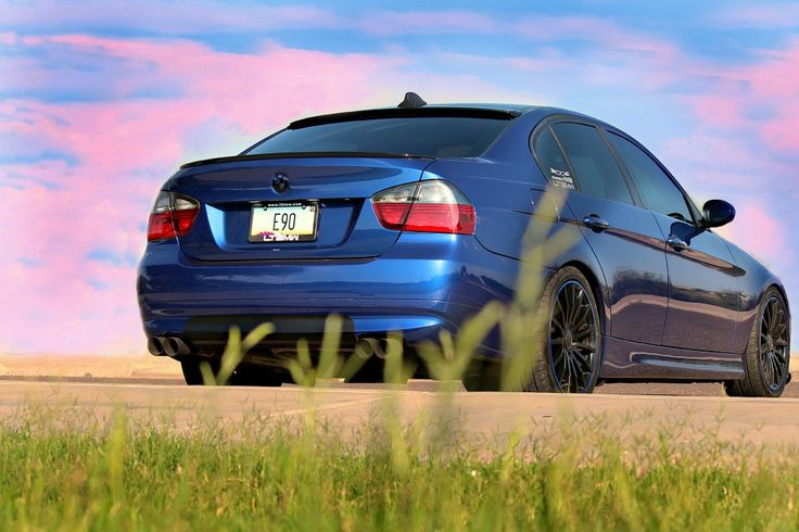 the blue car is parked on the side of the road in front of some tall grass