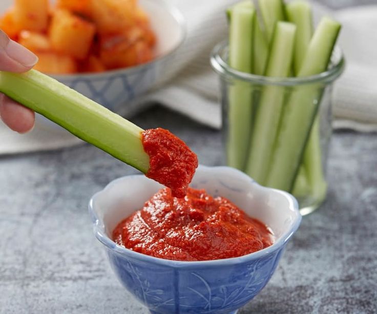 a person dipping something into a small blue bowl with celery and carrots in the background