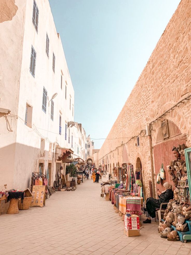 an alley way with people shopping and sitting on the benches in front of buildings that are made of stone