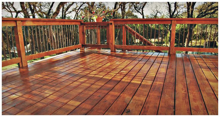 a wooden deck with railings and trees in the background