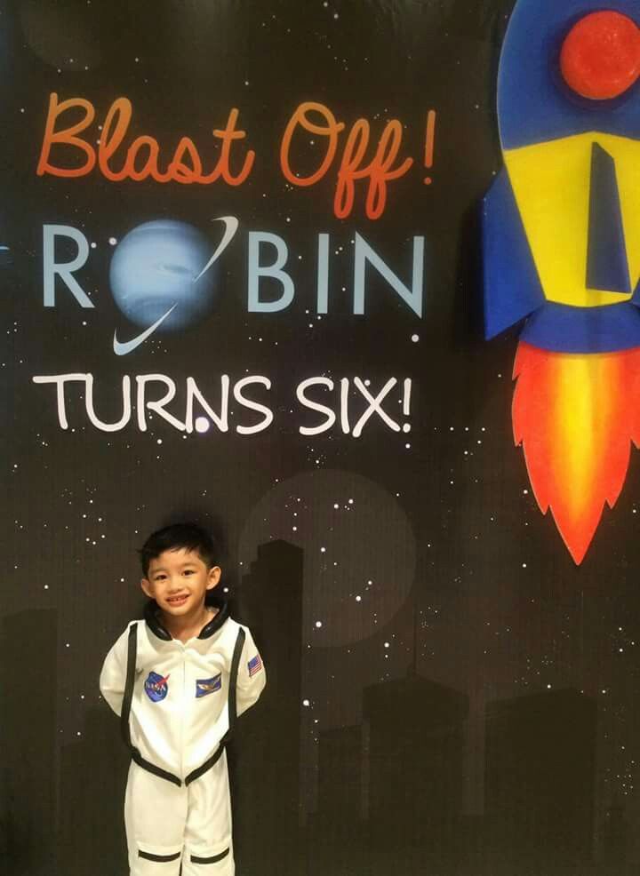 a young boy standing in front of a sign that says blast off robin turns six