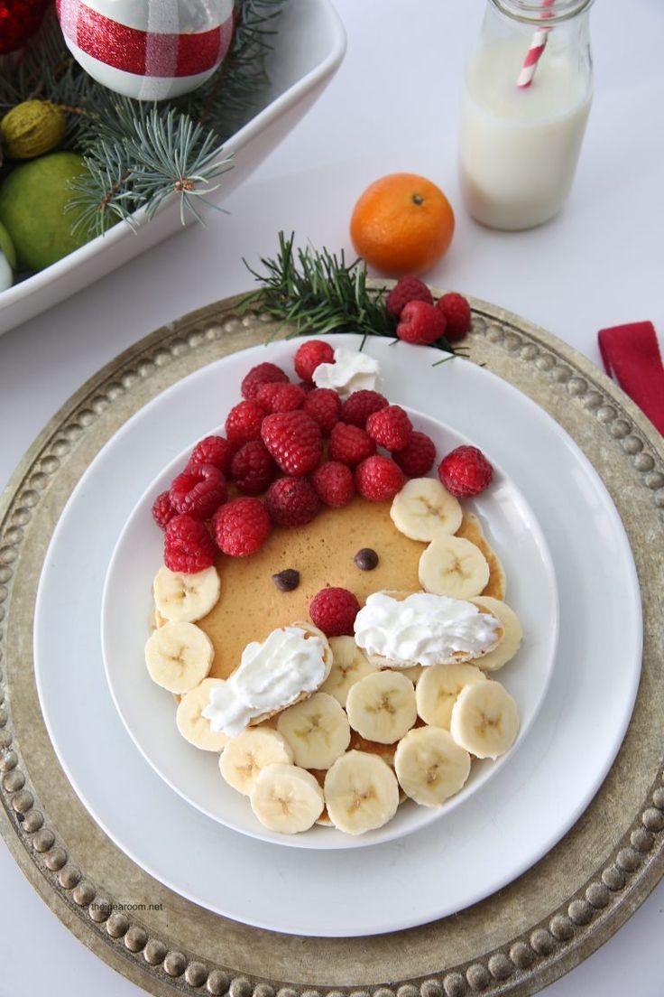 a white plate topped with pancakes covered in bananas and raspberries next to fruit