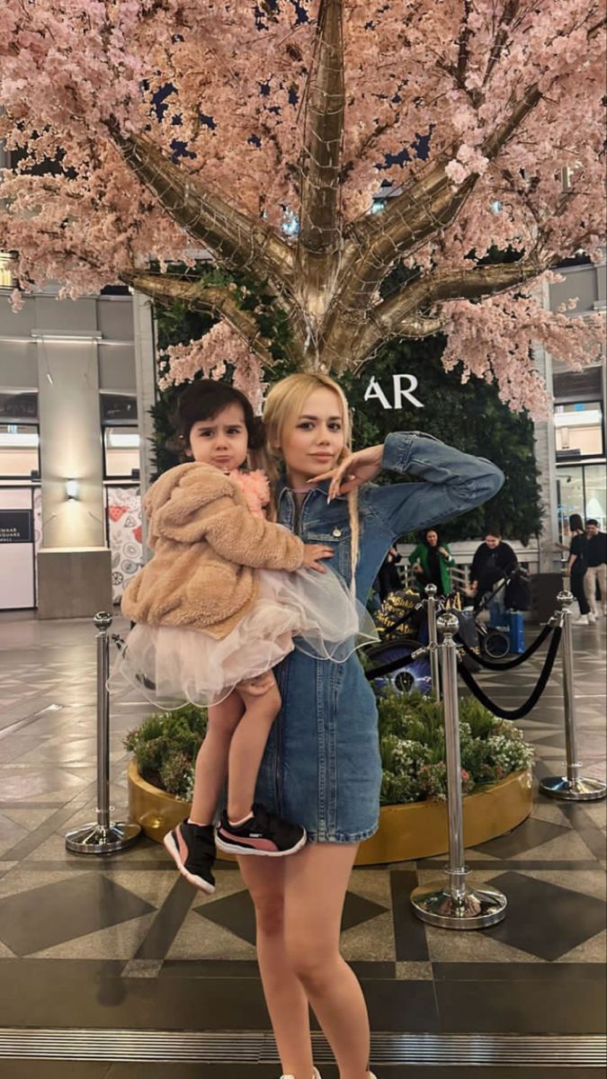 a woman holding a child in her arms while standing next to a tree with pink flowers