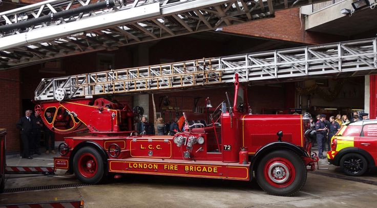 a red fire truck parked in front of a building with people standing around and looking at it