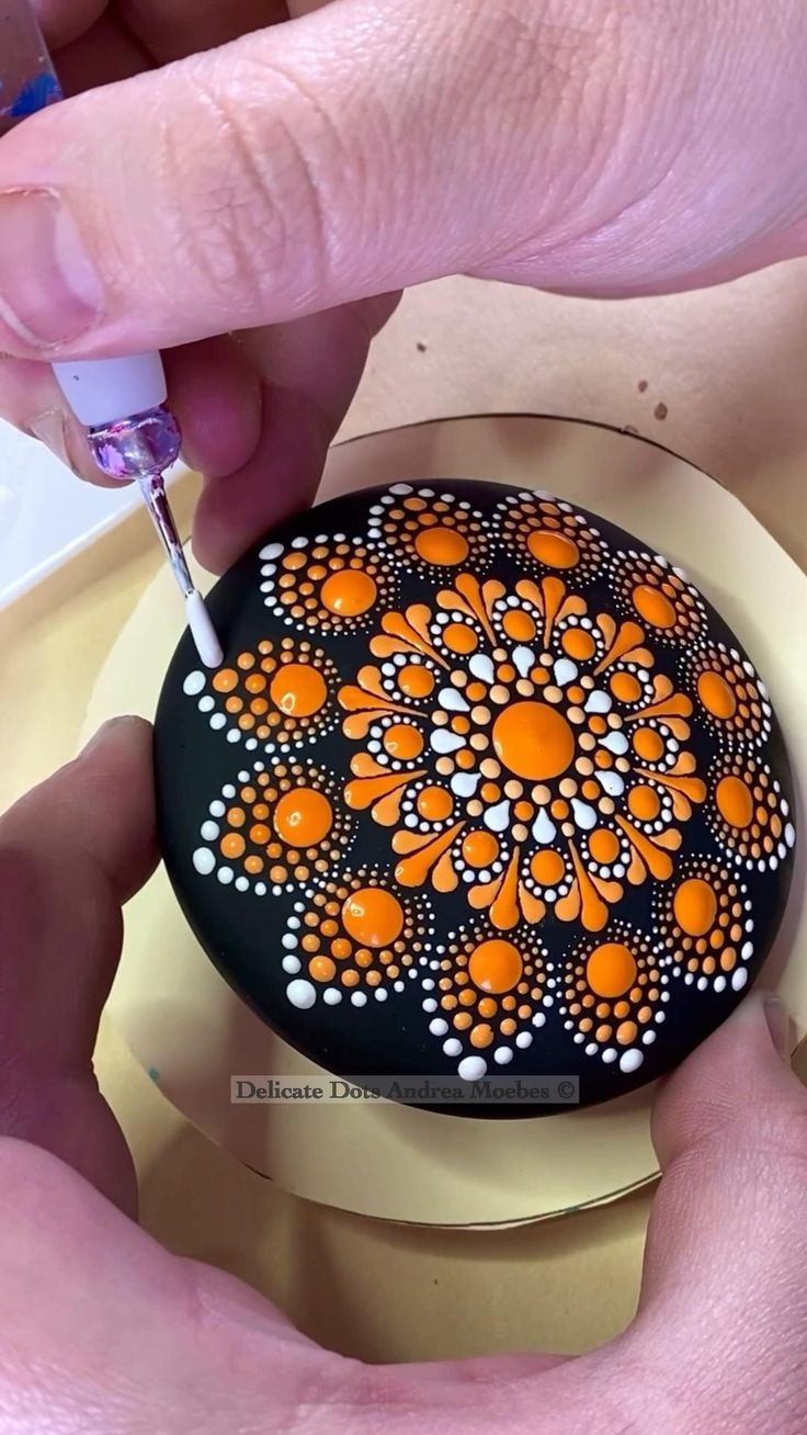 a person is painting an orange flower on a black and white plate with dots in the center