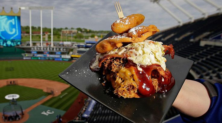 a person holding up a plate with food on it at a baseball game in the stadium