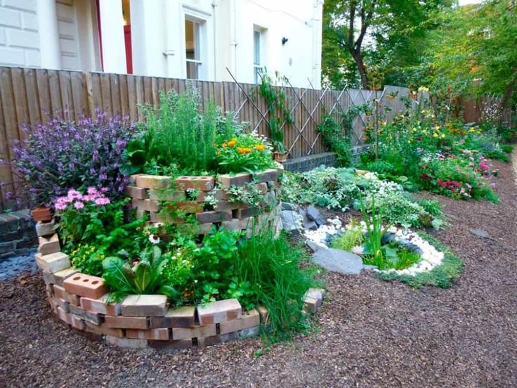 a garden with lots of different plants and flowers in the ground next to a fence