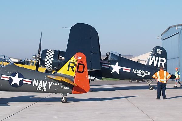 two navy planes parked on the tarmac with men standing around them looking at them