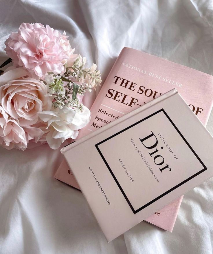 two pink books sitting on top of a bed next to a bouquet of white and pink flowers