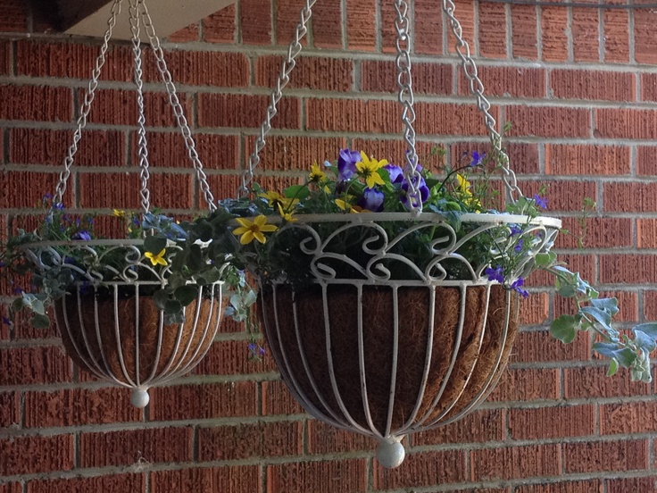 two hanging planters filled with flowers on a brick wall