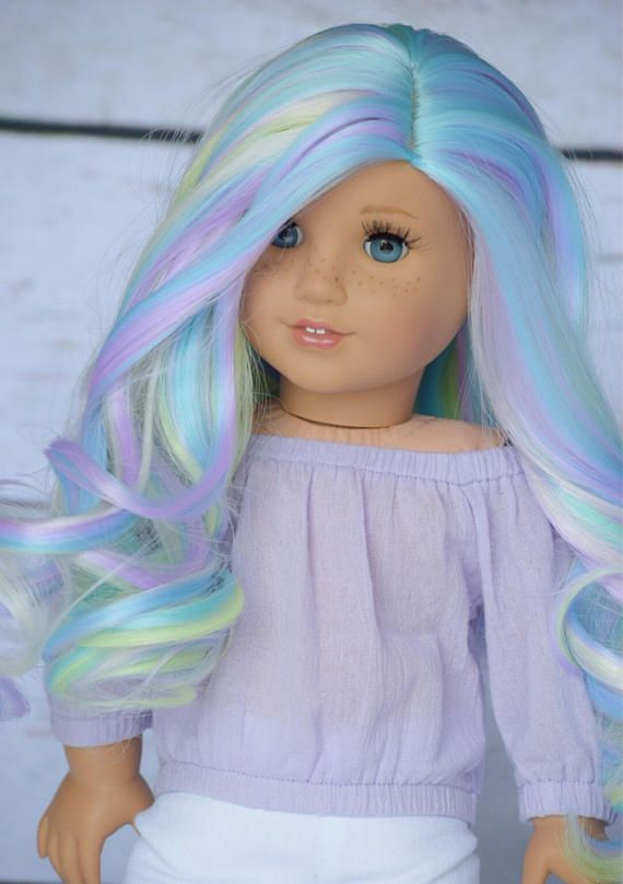 a doll with pastel blue, green and yellow hair is standing on a white surface