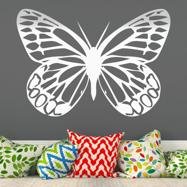 a white butterfly wall decal sitting on top of a bed next to colorful pillows