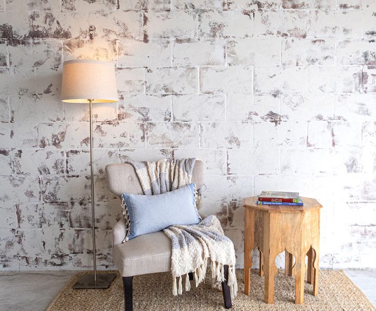 a chair sitting next to a table with a lamp on top of it and a rug in front of it