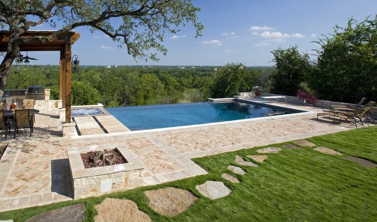 a backyard with a pool and fire pit surrounded by greenery, grass and trees