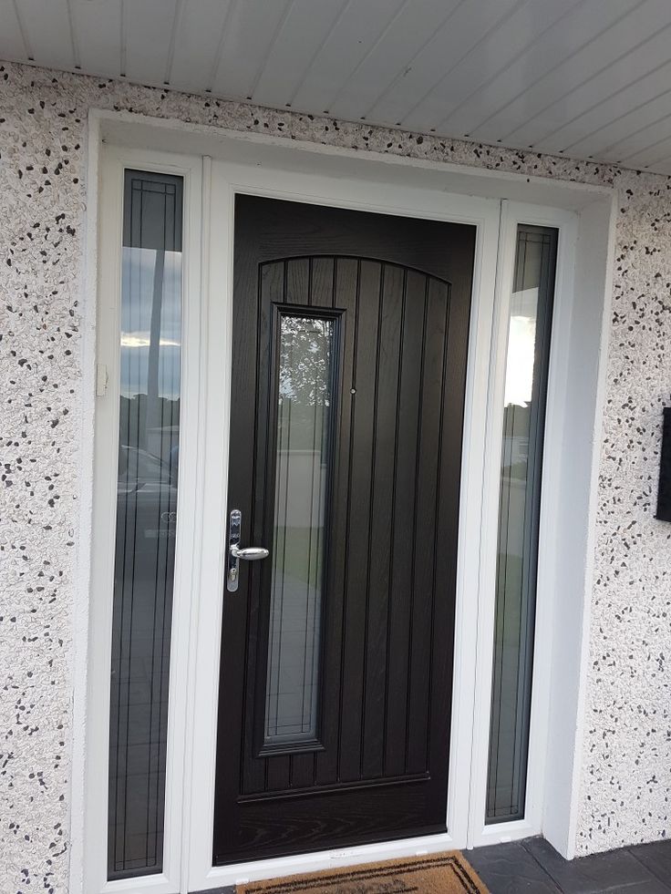 a black front door with two sidelights and a brown rug on the ground in front of it