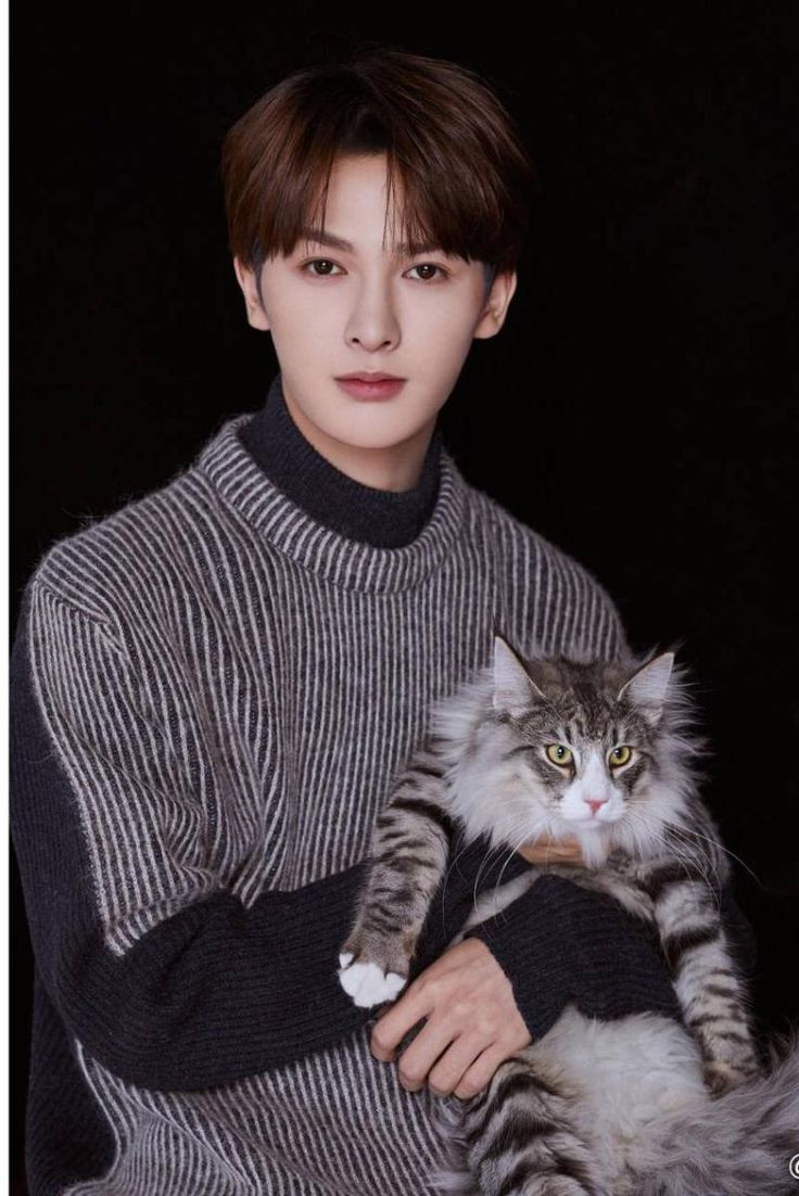 a woman holding a cat in her arms while wearing a turtle neck sweater and black pants