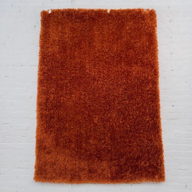 an orange shaggy rug on a white brick wall