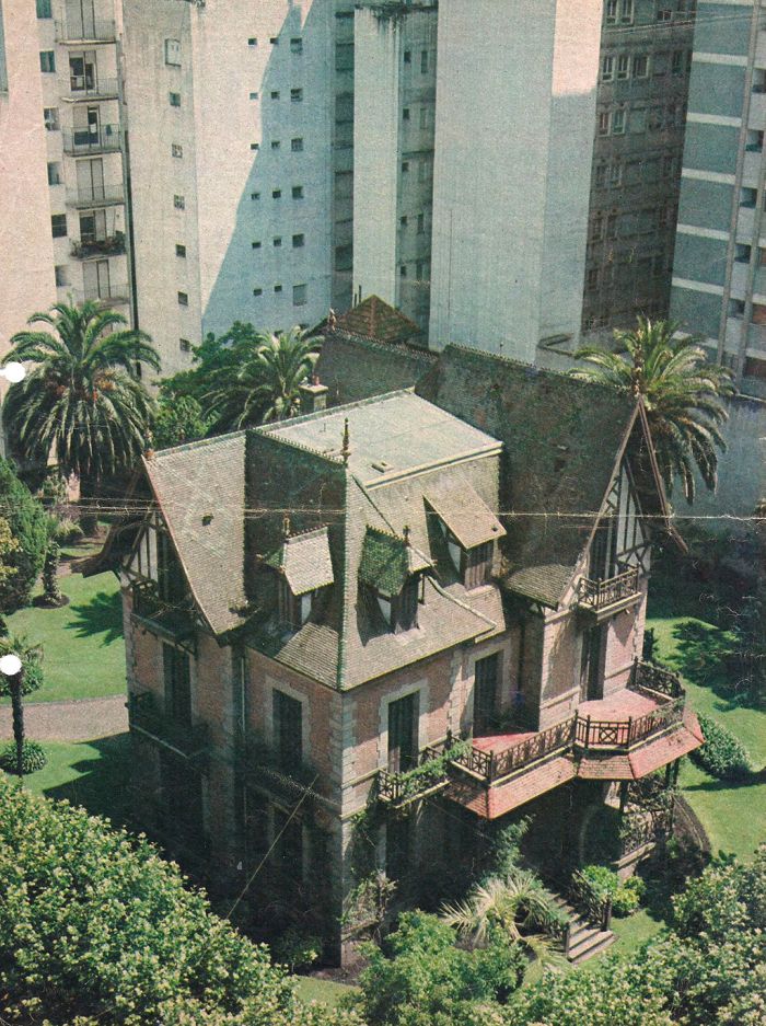 an aerial view of a house in the middle of some trees and buildings with balconies