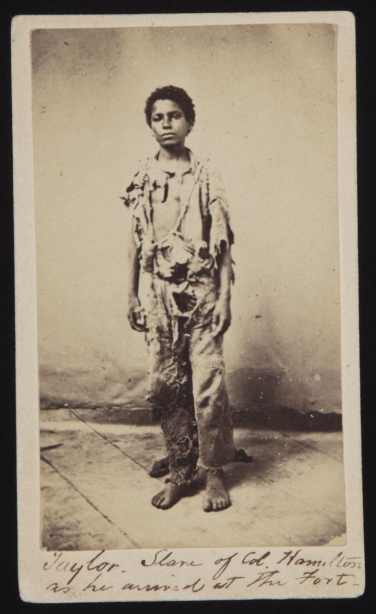 an old black and white photo of a young boy in overalls standing next to a wall