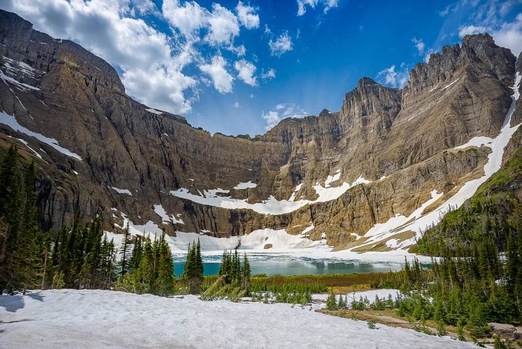 the mountains are covered in snow and surrounded by pine trees, with a lake below