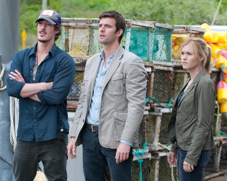 two men and a woman standing next to each other in front of lobster cages on the beach