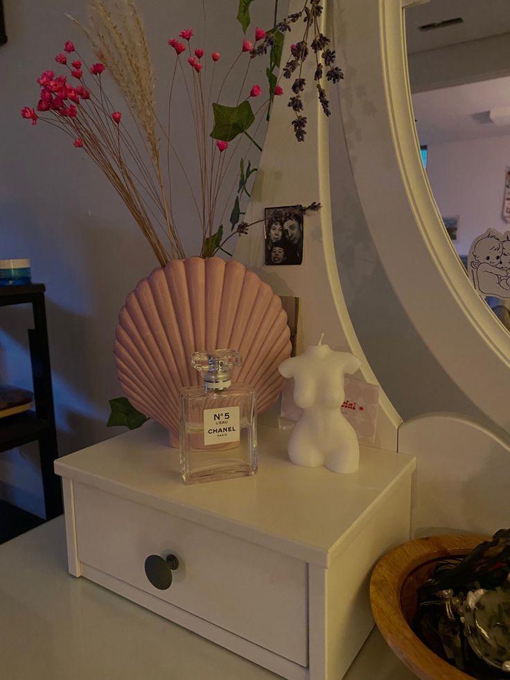 a white dresser topped with a bottle of perfume next to a vase filled with flowers