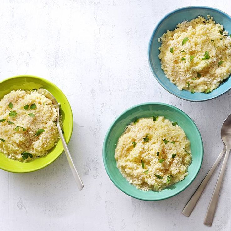 three bowls filled with food on top of a white table next to two spoons