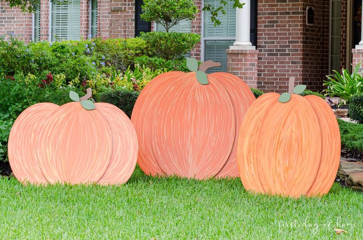 three orange pumpkins sitting in front of a brick house with green grass and bushes