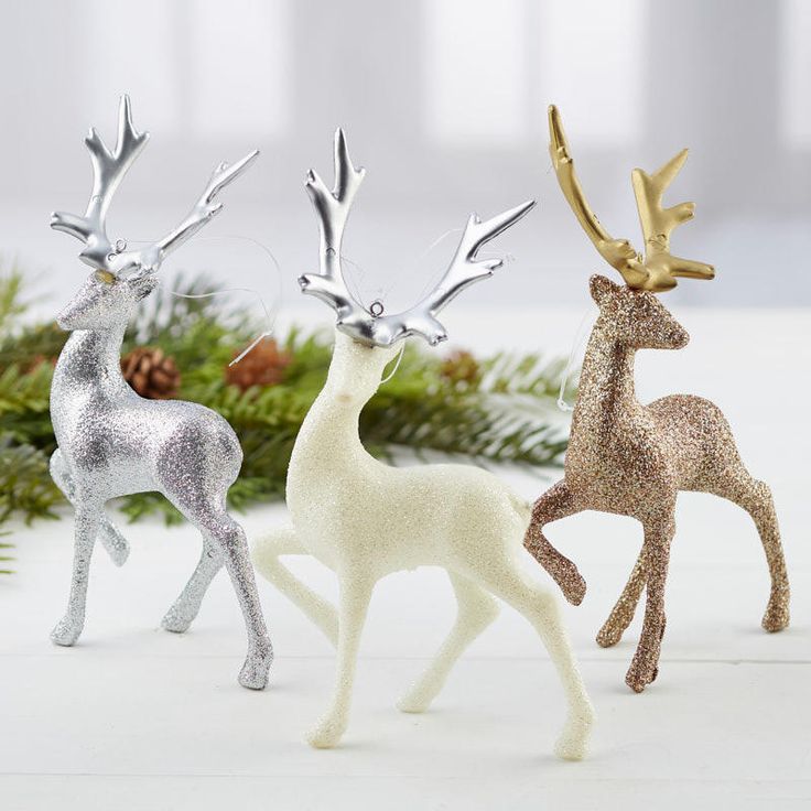 three silver and gold reindeer ornaments in front of pine branches