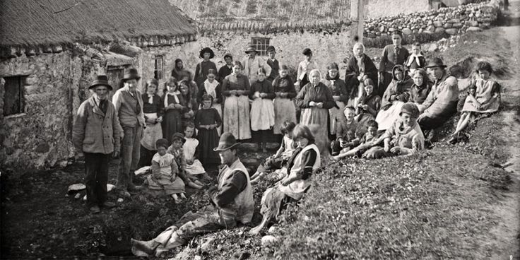 an old black and white photo of people posing for a group shot in front of some thatched houses