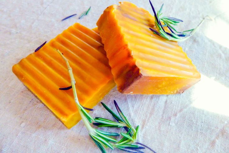 two pieces of cheese sitting on top of a white cloth covered in green leaves and rosemary