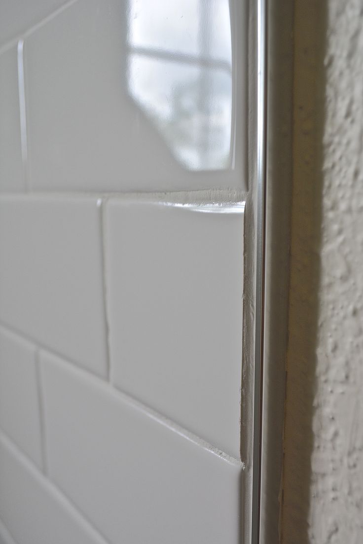 the corner of a bathroom with white tiles on the wall and door handle in front of it