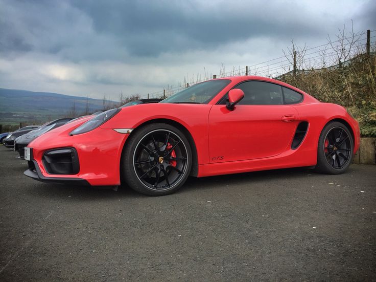 a red sports car parked in a parking lot next to other cars on a cloudy day