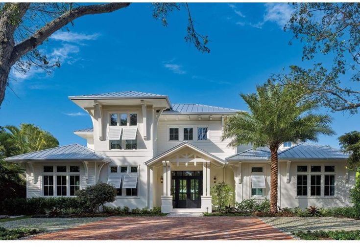 a large white house with lots of windows and palm trees in front of the entrance