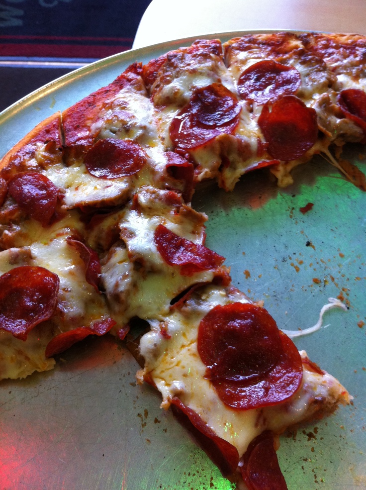 a half eaten pepperoni pizza sitting on top of a metal pan with one slice missing