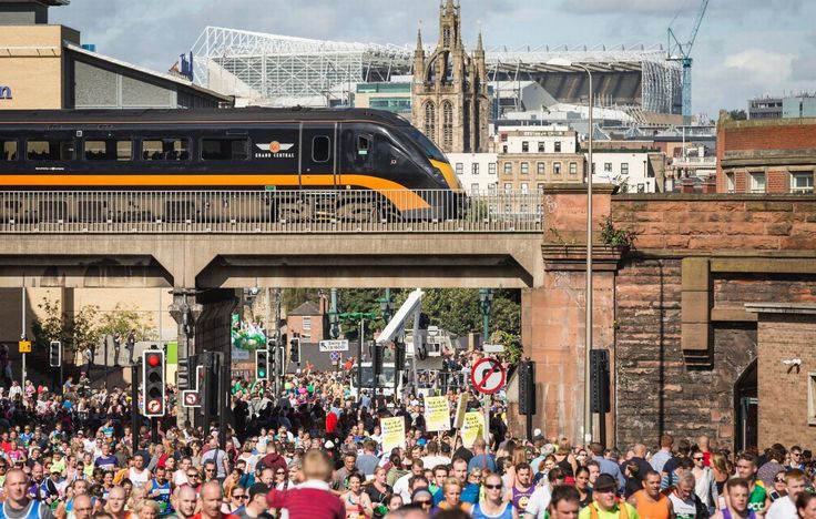 a crowd of people walking under a bridge with a train on it's track