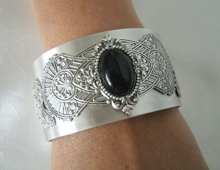 This beautiful silver plated cuff bracelet has a black onyx stone set on silver plated embellishments and silver plated gothic wings on the sides. Adjustable. Antique Black Wedding Jewelry, Elegant Cabochon Cuff Bracelet For Formal Occasions, Elegant Cabochon Cuff Bangle Bracelet, Ornate Metal Bangle Jewelry, Victorian Style Metal Jewelry With Jewels, Metal Bangle With Jewels, Elegant Black Jewelry With Intricate Design, Antique Adjustable Bangle Jewelry, Antique Adjustable Jewelry For Formal Occasions