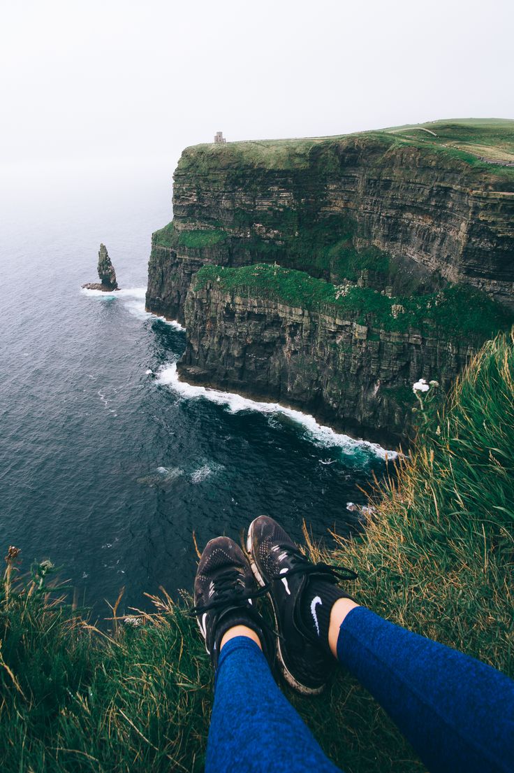 person's feet resting on the edge of a cliff overlooking an ocean with cliffs in the background