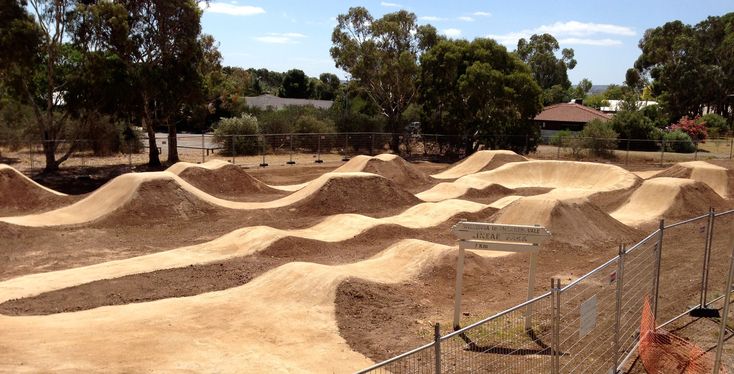 a group of skateboard ramps sitting in the middle of a dirt field next to a fence