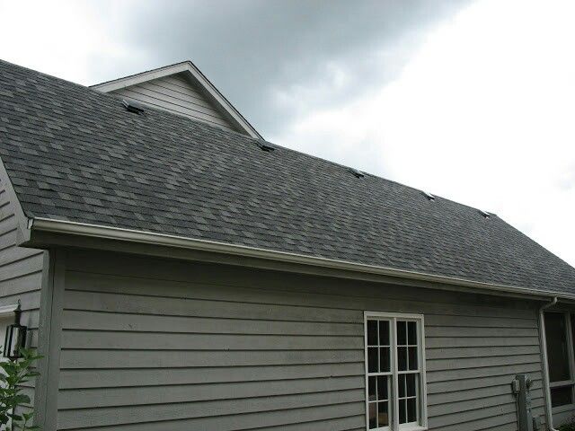 a house with a gray roof and white trim on the side of it, under a cloudy sky