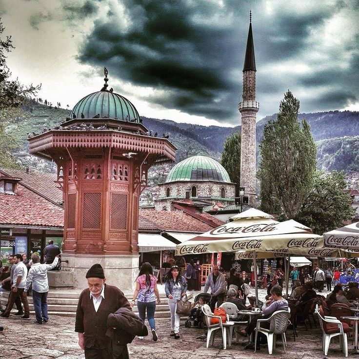 people are walking around an outdoor market with umbrellas and tables in the foreground