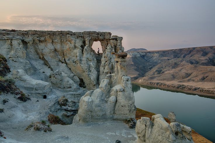 a large rock formation next to a body of water in the middle of a mountain range