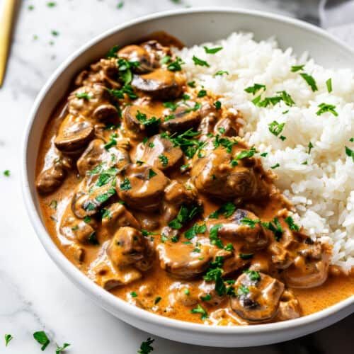 a white bowl filled with rice and meat covered in mushroom gravy on top of a table