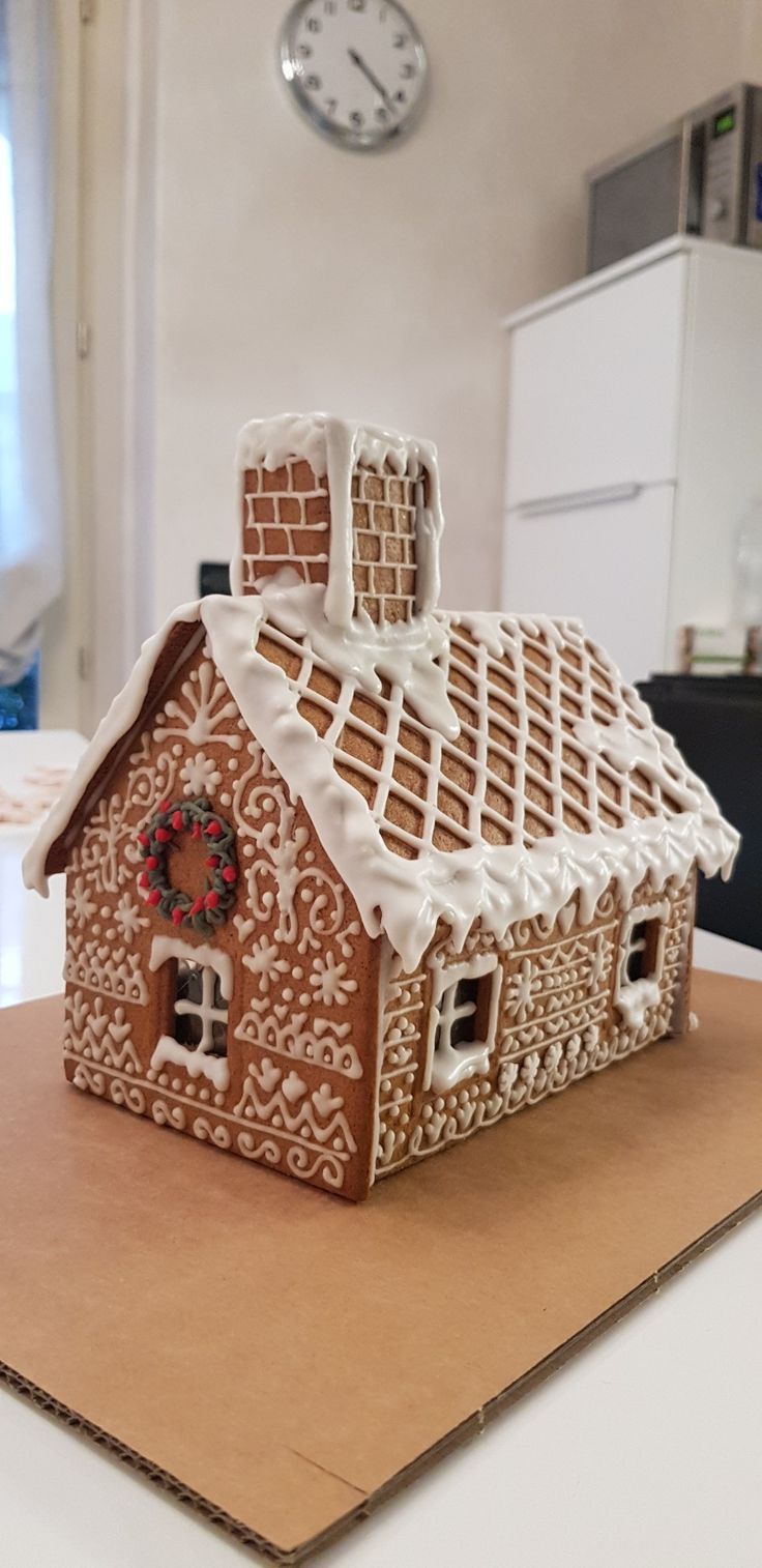 a gingerbread house is sitting on top of a cardboard board with a clock in the background