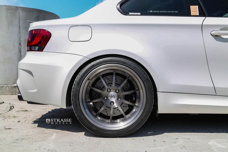 the rear end of a white car parked in front of a cement wall and water tank