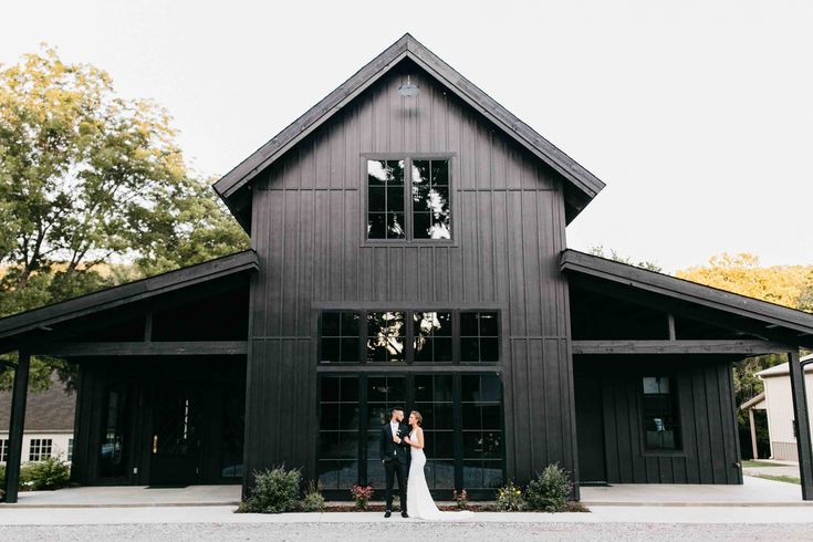 a bride and groom standing in front of a black barn with windows on each side