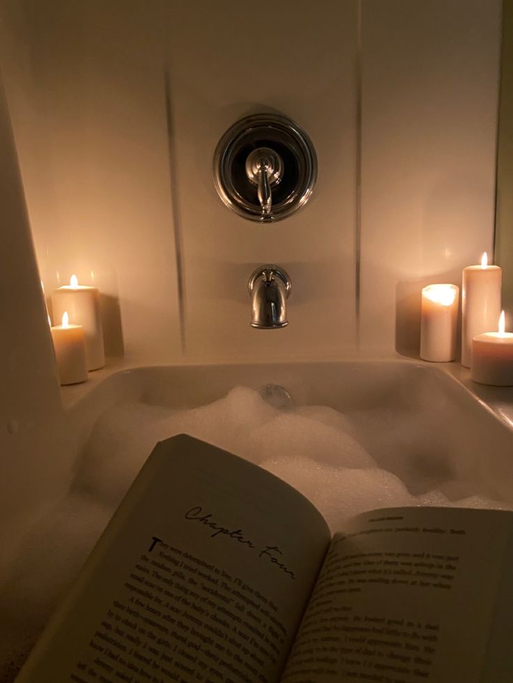 an open book sitting on top of a bath tub filled with water and candles next to it