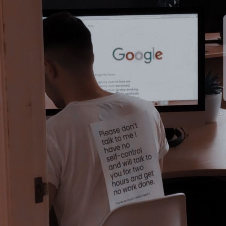 a man sitting in front of a computer with a sign on his t - shirt