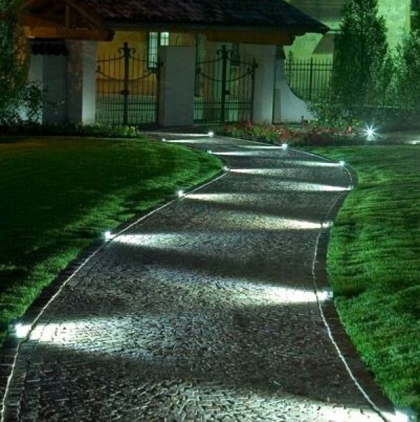 a pathway that is lit up in the night with light shining on it and grass around it